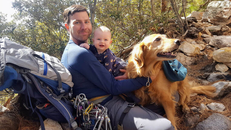 Justin Healy holding Kristina Waker's son while sitting next to his dog Leela.